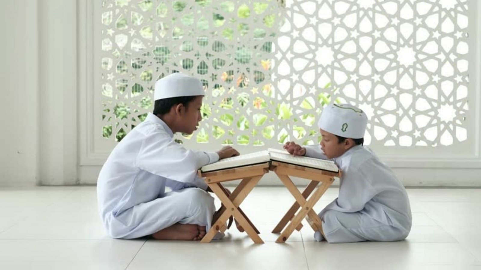 Two boys in white reading the Quran on wooden stands